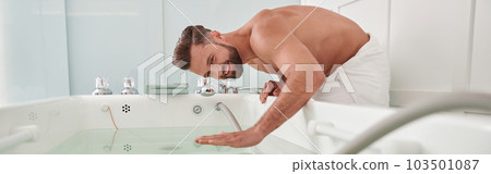 Smiling man with bare chest touches clear water in modern hydro massage tub in salon Smiling man with bare chest touches clear water in modern hydro massage tub in salon 103501087