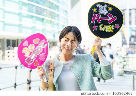 A woman standing in front of a live venue holding a cheering fan Oshikatsu A woman standing in front of a live venue holding a cheering fan Oshikatsu 103502402