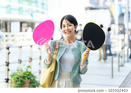A woman standing in front of a concert venue with a cheering fan Oshikatsu 103502403