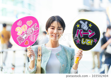 A woman standing in front of a concert venue with a cheering fan Oshikatsu 103502404
