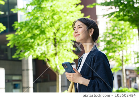 A woman walking in a green city with a smartphone 103502484
