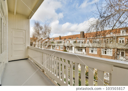 a balcony with white railings and brick buildings in the background on a sunny day, there is a blue sky 103503817