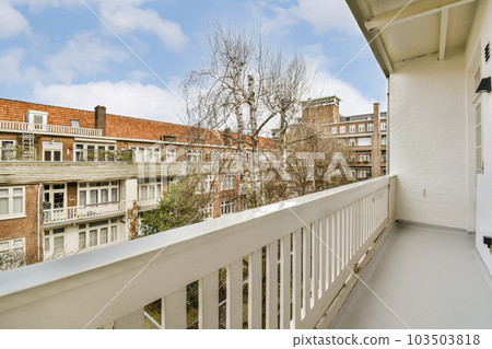 a balcony with white railings and brick buildings in the background, there is a tree on the right side a balcony with white railings and brick buildings in the background, there is a tree on the right side 103503818