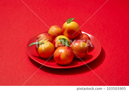 A dish in round-shaped containing several peaches, put on red background. Peach (Prunus persica) may help improve and protect your skin A dish in round-shaped containing several peaches, put on red background. Peach (Prunus persica) may help improve and protect your skin 103503905