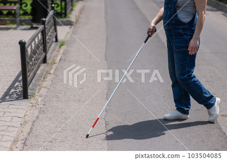 Blind pregnant woman crosses the street with the help of a tactile cane. 103504085