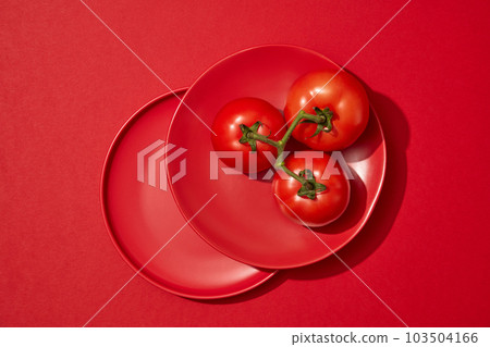 Two red dishes stacked on each other with three tomatoes put on top. Tomato (Solanum lycopersicum) helps in maintaining a proper pH level for your skin 103504166