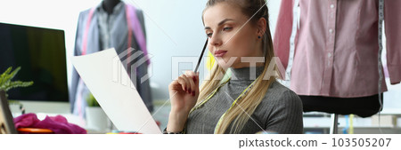 Woman designer are considering sketches of clothes at workplace in atelier 103505207