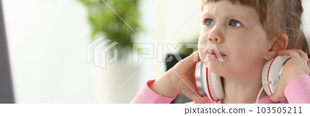 Portrait of a little beautiful child girl carefully looks at monitor in headphones Portrait of a little beautiful child girl carefully looks at monitor in headphones 103505211