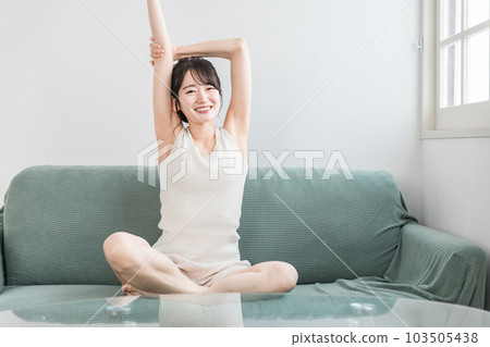 年輕的亞洲女性在家裡的沙發上放鬆和提神(早上的例行公事) 年輕的亞洲女性在家裡的沙發上放鬆和提神(早上的例行公事) 103505438