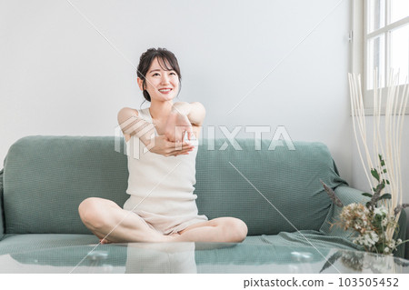 年輕的亞洲女性在家裡的沙發上做輕度伸展運動、體操和瑜伽(早上例行活動) 年輕的亞洲女性在家裡的沙發上做輕度伸展運動、體操和瑜伽(早上例行活動) 103505452