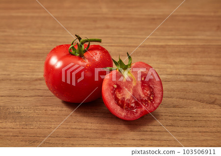 Front view of a ripe fresh tomato and halves of tomato on wooden table. The nutritional composition of tomatoes can protect the body from many dangerous diseases.  103506911