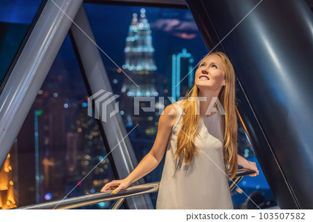 Woman looks at Kuala lumpur cityscape. Panoramic view of Kuala Lumpur city skyline evening at sunset skyscrapers building in Malaysia Woman looks at Kuala lumpur cityscape. Panoramic view of Kuala Lumpur city skyline evening at sunset skyscrapers building in Malaysia 103507582