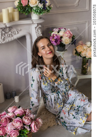 Beautiful young woman sitting in a room among the flowers 103508078