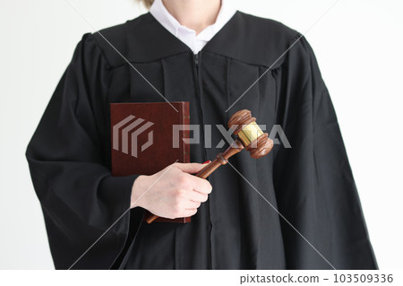 Woman judge in classic gown holds book and wooden mallet Woman judge in classic gown holds book and wooden mallet 103509336