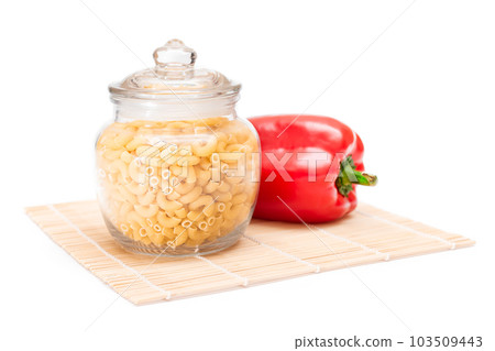 Uncooked Chifferi Rigati Pasta in Glass Jar and Red Bell Pepper on Bamboo Mat Isolated 103509443