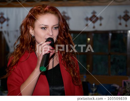 Red haired woman event host speaks with a microphone in a dark room 103509839