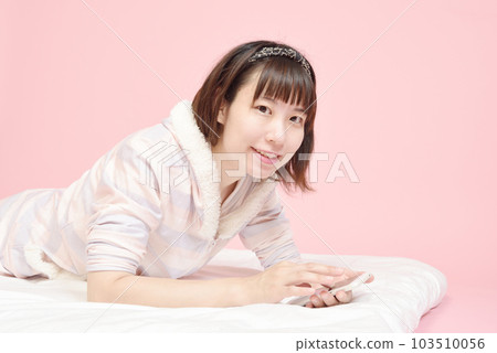 A woman in pajamas who operates a smartphone 103510056