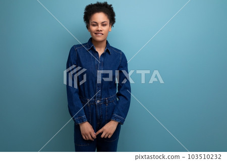 portrait of a young woman with dark skin and black curly hair dressed in blue denim overalls 103510232