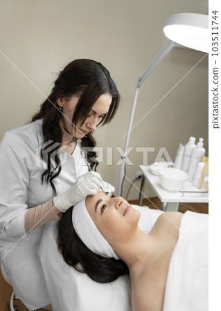 The photo reflects the therapeutic procedure of deep cleansing of the skin of the face, during which a beautiful woman finds harmony and relaxes in a beauty clinic. Cosmetologist works in the office 103511744