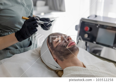 Dermatologist applies a green mask to the girl's face, after carbon peeling. 103512258