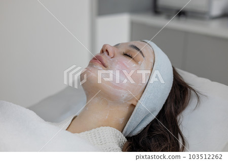 Astonishing brunette with white cream mask on face lies in beauty health clinic. Astonishing brunette with white cream mask on face lies in beauty health clinic. 103512262