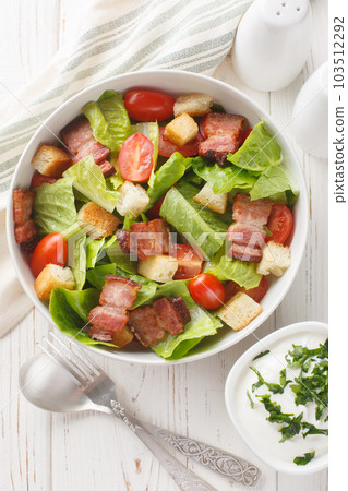 BLT salad is loaded with fresh lettuce, crispy bacon, bright tomatoes croutons closeup on the plate. Vertical top view BLT salad is loaded with fresh lettuce, crispy bacon, bright tomatoes croutons closeup on the plate. Vertical top view 103512292
