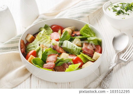 BLT Salad has a homemade ranch dressing, crispy bacon, croutons, lettuce and tomato closeup on the plate. Horizontal 103512295