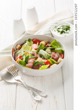 BLT salad is loaded with fresh lettuce, crispy bacon, bright tomatoes croutons closeup on the plate. Vertical 103512297