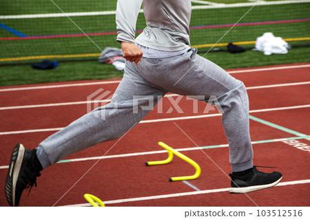 Legs of runner running over yellow mini hurdles on a red track 103512516