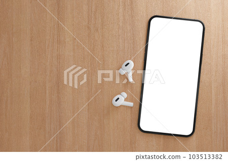Modern smartphone with blank white screen with wireless earphones on wooden table. Mockup TWS earbuds with smartphone on wood background. copy space 103513382