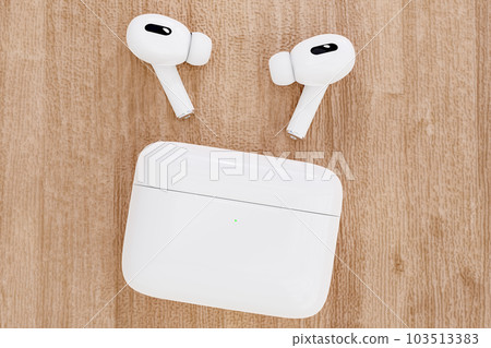 Closeup white TWS true wireless stereo earbuds and case on wooden table background. Closeup modern headphone Closeup white TWS true wireless stereo earbuds and case on wooden table background. Closeup modern headphone 103513383