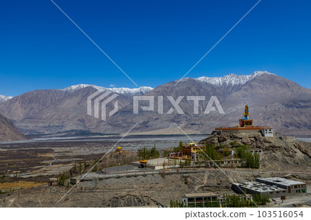 Big Sitting Buddha Statue at Diskit Monastery with Himalaya Range in the back - Nubra Valley, Ladakh, India. 103516054