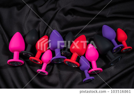 A set of silicone anal plugs in different colors and sizes on a black silk sheet. A set of silicone anal plugs in different colors and sizes on a black silk sheet. 103516861