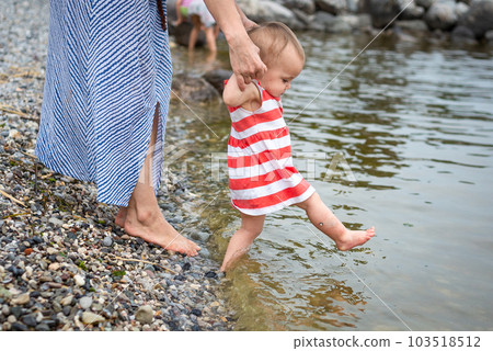 close up view on baby in striped dress making steps in water being held by motherhands close up view on baby in striped dress making steps in water being held by motherhands 103518512