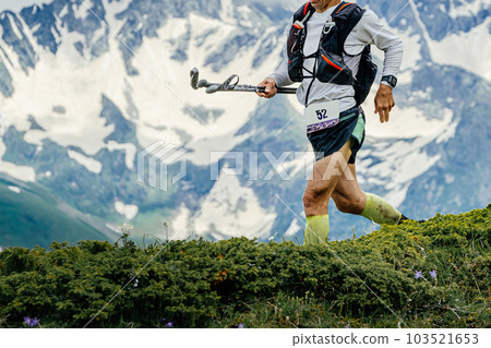 athlete runner running skyrunning trail race on green meadow in background snowy mountain, trekking poles in hand athlete runner running skyrunning trail race on green meadow in background snowy mountain, trekking poles in hand 103521653