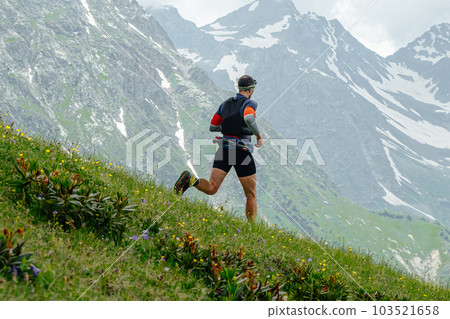male athlete runner running down mountain marathon race on green meadow, background snowy peaks male athlete runner running down mountain marathon race on green meadow, background snowy peaks 103521658