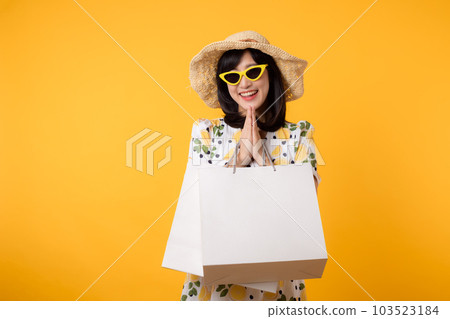 Portrait happy attractive young asian woman with trendy springtime dress, hat, sunglasses fashion and paper bag isolated on yellow background. Summertime sale shopping concept. 103523184