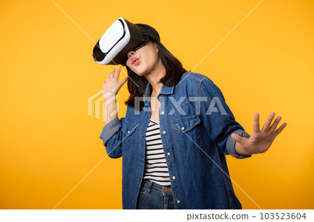 Young asian woman get experienced wearing virtual reality headset game entertainment isolated on yellow background. Winner of cyber future video game concept. Young asian woman get experienced wearing virtual reality headset game entertainment isolated on yellow background. Winner of cyber future video game concept. 103523604