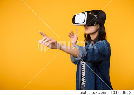 Young asian woman get experienced wearing virtual reality headset game entertainment isolated on yellow background. Winner of cyber future video game concept. 103523690