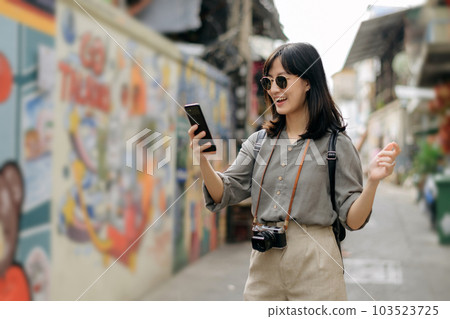 Young Asian woman backpack traveler using mobile phone, enjoying street cultural local art wall. Traveler checking out side streets. Young Asian woman backpack traveler using mobile phone, enjoying street cultural local art wall. Traveler checking out side streets. 103523725