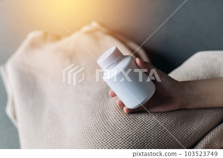 pain ill sick young female adult person hand hold pill medicine bottle over a blanket on bed. disease, health, medical, treatment pharmacy, vitamin, supplement take care concept. pain ill sick young female adult person hand hold pill medicine bottle over a blanket on bed. disease, health, medical, treatment pharmacy, vitamin, supplement take care concept. 103523749