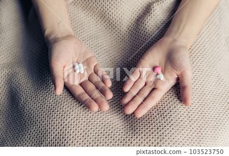Female hands hold and offer two choice medicine pills capsule for chosen. White and pink candy or meds compare to choose from. Concept decision making or indecisiveness. Female hands hold and offer two choice medicine pills capsule for chosen. White and pink candy or meds compare to choose from. Concept decision making or indecisiveness. 103523750
