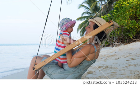 Happy mother swinging with her adorable baby on beach swings on tropical island in Maldives 103524218