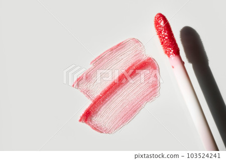 Smears of shining lip gloss and lip gloss brush on white background, hard shadows 103524241