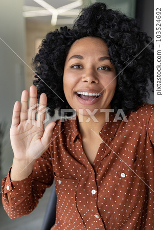 Vertical shot, young beautiful african american business woman with curly hair talking on video call, waving at smartphone camera, using remote communication app. 103524692