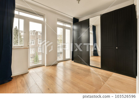 an empty room with wood flooring and black closets on either side of the room, looking out onto the street 103526596