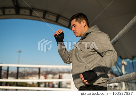 A man in a hoody trains in boxing at the stadium.  103527827