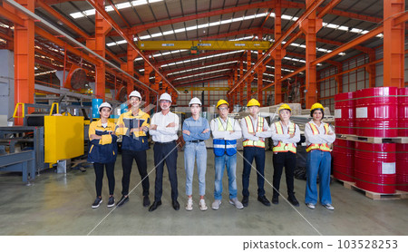 Group of male and female factory labor stand smiling together with arms crossed in industry factory. Everyone wearing safety uniform and helmet. Workers working in the metal sheet factory. 103528253