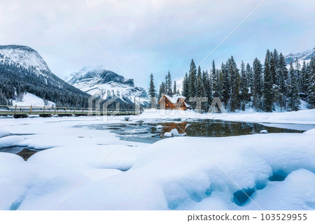 Frozen Emerald Lake with wooden lodge in pine forest on winter Frozen Emerald Lake with wooden lodge in pine forest on winter 103529955