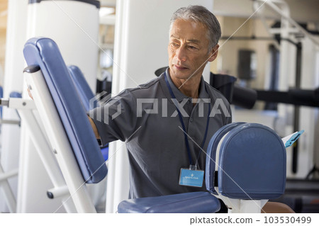 Middle-aged gym staff checking training machines at the gym Middle-aged gym staff checking training machines at the gym 103530499